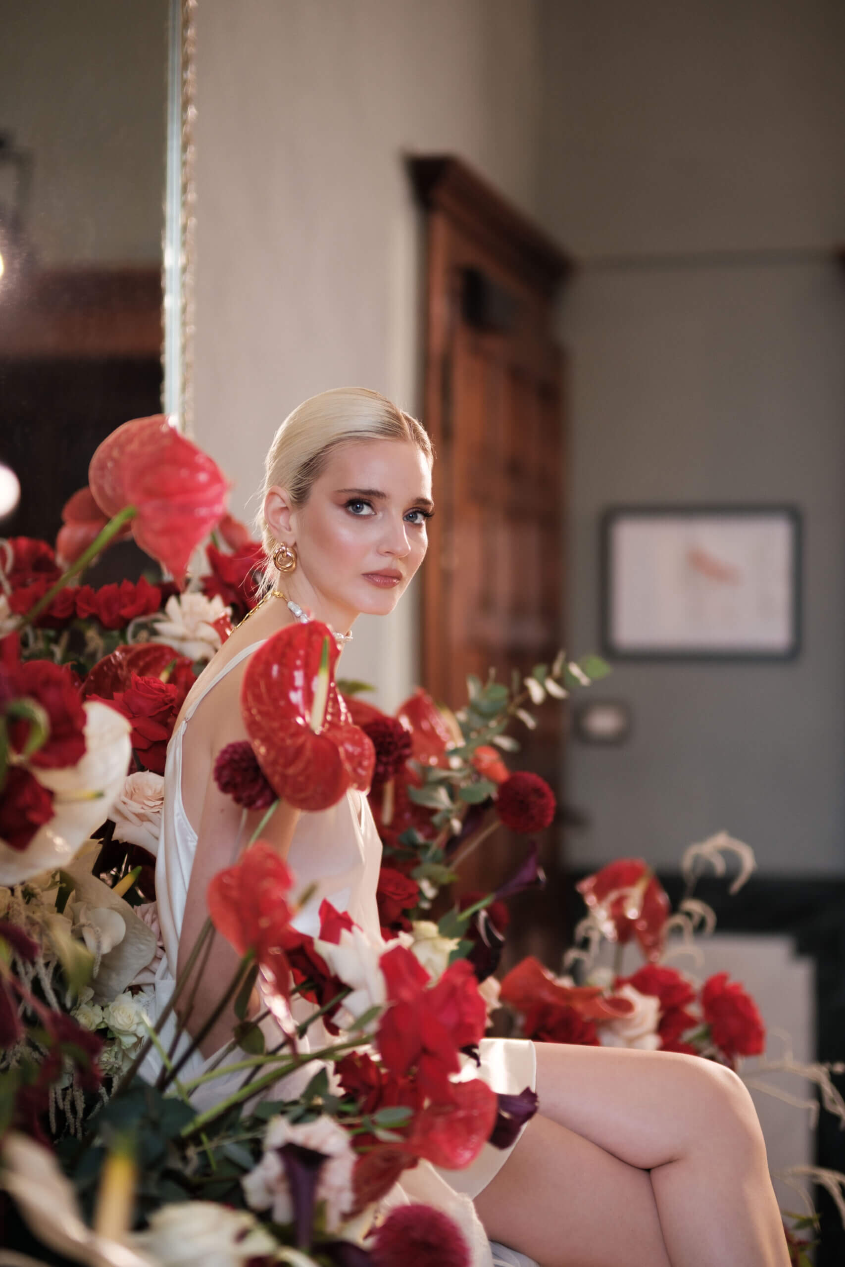 Braut im Seidenkleid zwischen roten Anthurien und Rosen